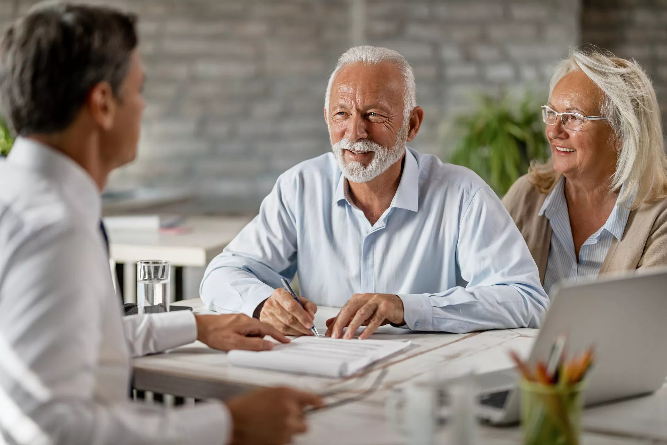happy-senior-couple-signing-an-agreement-while-having-a-meeting-with-financial-advisor-1184000441-2125x1416